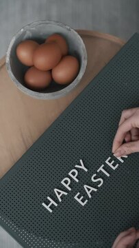 close-up vertical video of a person arranging the text "Happy Easter" on a plain background with an eggs, 
