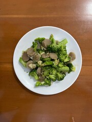 A plate of stir fry broccoli with garlic and sliced meatballs on wood table background