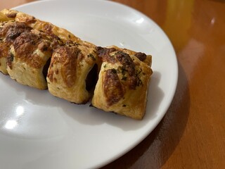 Freshly baked puff pastry sausage rolls with parsley on a white plate, English party food, horizontal view from above