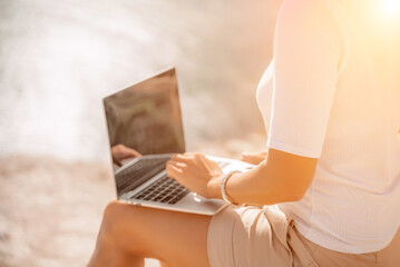 Fototapeta premium Freelance women sea working on the computer. Good looking middle aged woman typing on a laptop keyboard outdoors with a beautiful sea view. The concept of remote work.
