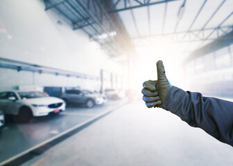 Auto mechanic signaling OK with a confident thumbs up gesture inside a car maintenance service...