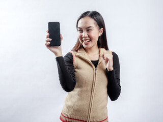 Portrait of an Indonesian Asian woman, wearing a light brown sweater, posing while showing her phone screen, isolated against a white background.
