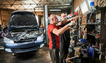 Side view of two men working in garage, auto, servicing center. Professional workers, repairmen, mechanics fixing, repairing car, holding equipment. Concept of manual labor.