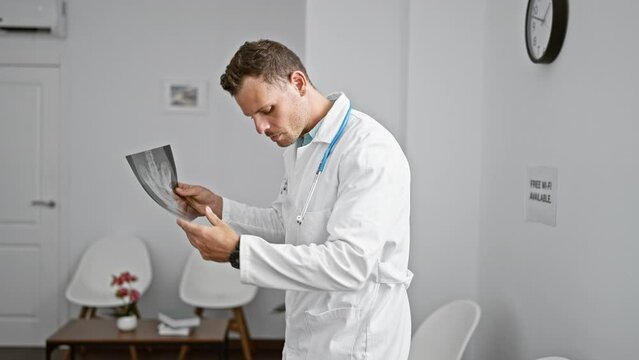Concentrated male doctor in white coat reviewing an x-ray in a modern clinic's examination room.