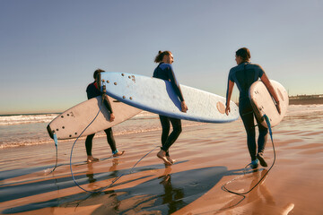 Group of friends with surfboards entering towards ocean for surfing on waves. High quality photo 