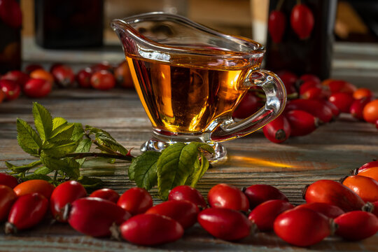 Rosehip oil in glass creamer. Against background of ripe berries. Rosae pingue fructuum oil. Rosae oleum. Rosehip. Rosa canina. Selective focus, close-up. Alternative medicine, home remedies