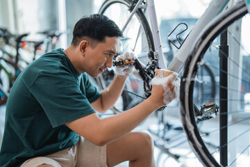 asian man washes bicycle gears with foaming soap at a bicycle shop