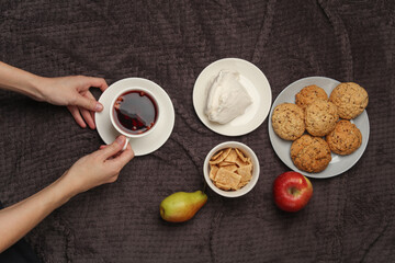 Female hands holding a cup of tea and breakfast in bed on a dark blanket