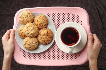 Hands holding a tray with tea and cookies over the bed