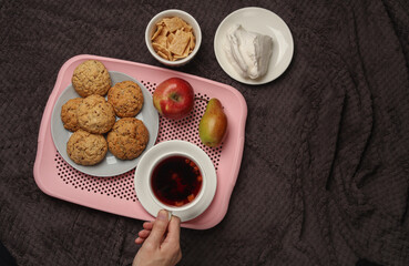 Female hands holding a cup of tea and breakfast in bed on a dark blanket