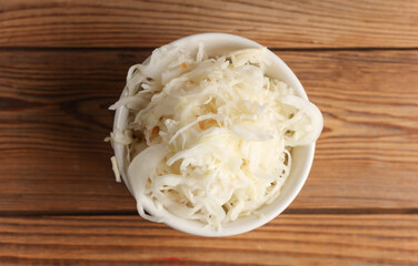 Sauerkraut in a ceramic bowl on a wooden background. Top view
