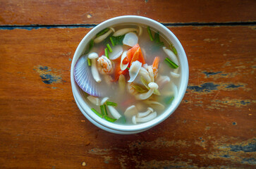 Seafood Tom Yam, Thai Clear soup in white bowl on Wooden table Background. Tom yum goong nam sai, clear stock broth version of Famous Thai soup with prawns