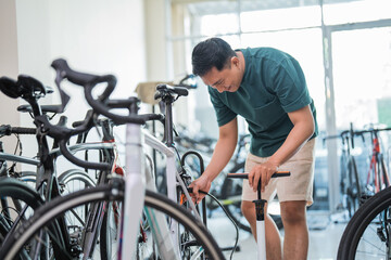 young Asian man pumping up the rear tire of a bicycle at a bicycle shop