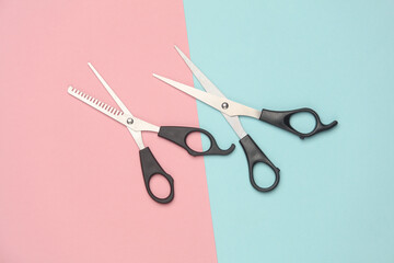 Two pairs of haircutting scissors on a pink blue background