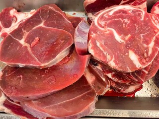 Close-up of fresh raw beef slices displayed at a butcher shop, showcasing the rich red color, marbling, and texture of the meat.