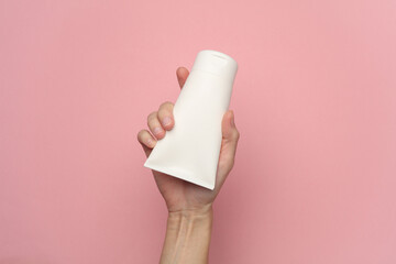 Female hand holding a white cream tube on a pink background