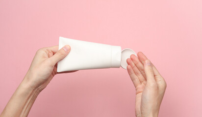 Female hands holding a white cream tube on a pink background - obrazy, fototapety, plakaty