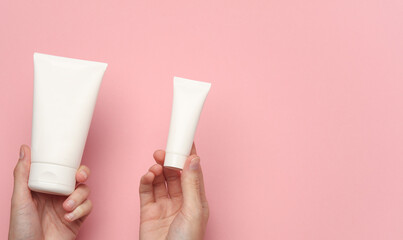 Female hands holding a white cream tubes on a pink background