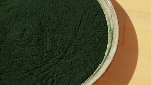 Rotating Organic blue-green algae spirulina powder food in plate. Health benefits of spirulina chlorella. Vitamins and minerals to diet. Detox dietary supplement Seaweed superfood concept