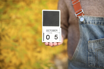 Woman holding calendar with date October 05 on yellow leaves background