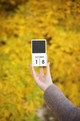 Woman holding calendar with date October 18 on yellow autumn leaves background