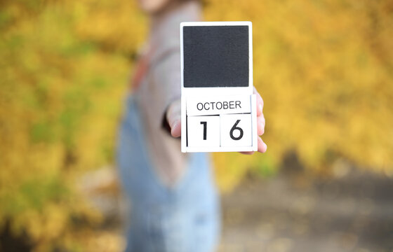 Woman holding calendar with date October 16 on yellow autumn leaves background