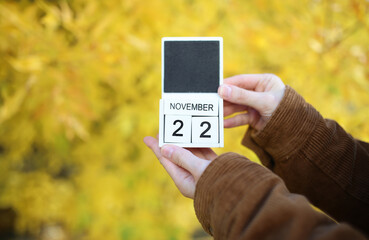 Woman holding calendar with date november 22 on yellow autumn leaves background