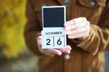 Woman holding calendar with date november 26 on yellow autumn leaves background