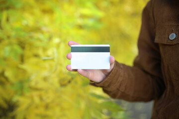 Hands holding credit card against the background of autumn trees