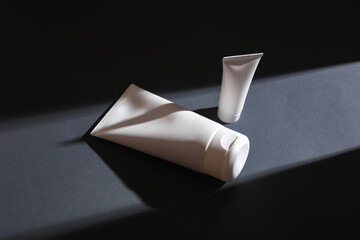 Cream tubes on gray background with stripe of light and shadow. Minimalism. Beauty concept