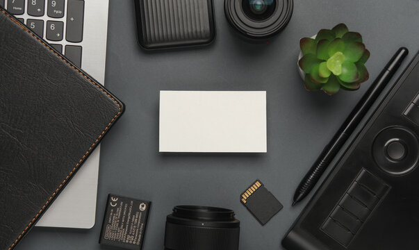White business card on a white background with a camera, notepad and modern accessories and gadgets on a dark gray background