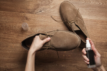 Hands apply water-repellent spray to suede shoes on the floor. Top view. Shoe care
