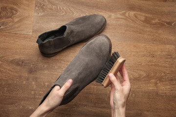 Hands cleaning suede shoes with a brush on the floor. Top view. Shoe care
