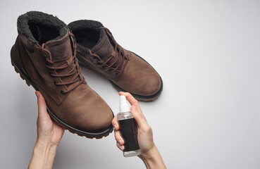 Hands apply water-repellent spray to nubuck boots on white background Top view. Shoe care