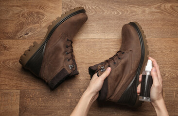 Hands apply water-repellent spray to nubuck boots on the floor. Top view. Shoe care