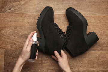 Hands apply water-repellent spray to suede shoes on floor. Top view. Shoe care