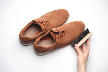 Hands cleaning suede shoes with a brush on white background. Top view. Shoe care