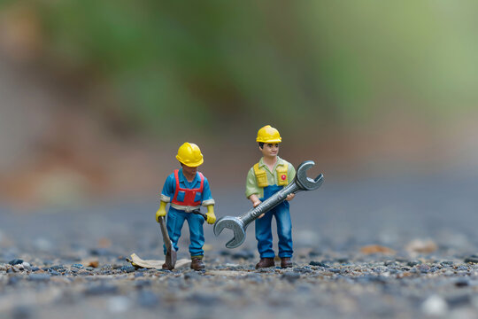 miniature workers carry a large wrench across a road