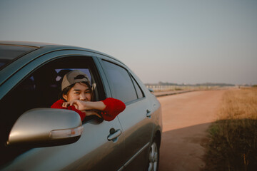 Young Asian woman in red sweater leaning out of car window looking out to the field.