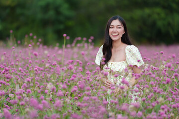 Fototapeta na wymiar beautiful woman in dress enjoying blooming pink globe amaranth or bachelor button field