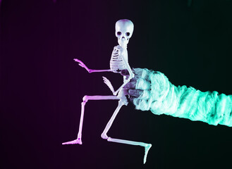 Mummy hand holding skeleton in neon light. Halloween concept