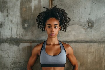 Confident female athlete with crossed arms standing against a textured grey background, showcasing fitness and determination.