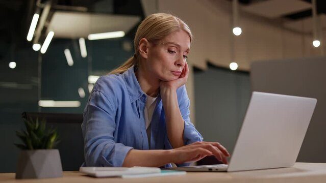Sleepy woman in shirt sitting with closed eyes at desk with laptop and dreaming about vacation. Female employee displeased with boring work and lazily typing on portable computer and looking tired.