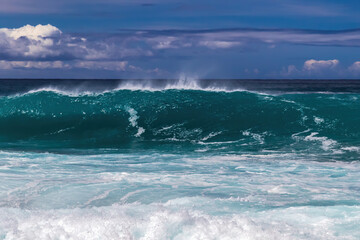 Large wave breaking offshore, Kona coast, Big island of Hawaii. Blue sky and clouds in background.
