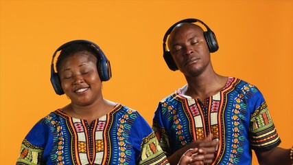 Cheerful ethnic people playing air guitar with music on headset, having fun pretending to use musical instrument and listen to groovy tunes. African american couple enjoying jam session.