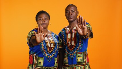 Confident ethnic couple showing stop sign in studio, raising palm and expressing their rejection....