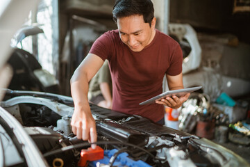 young male mechanic wiring a battery while using a digital tablet at a repair shop