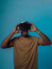 In a futuristic visual, an African American man stands isolated against a striking blue backdrop, adorned with VR glasses that transport him into a cutting-edge virtual reality experience, merging