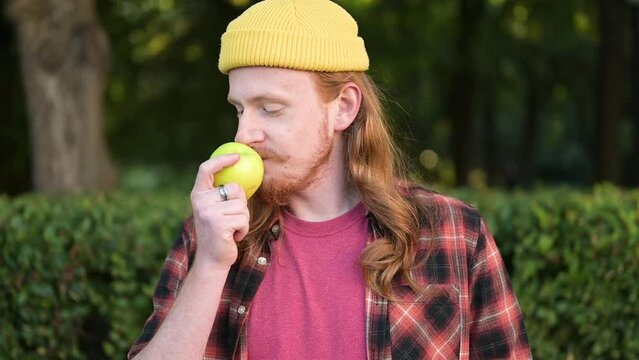 Close-up of a stylish red-haired guy in a yellow hat with a ripe green apple. The image of a man who loves fruits. Veganism and vegetarianism