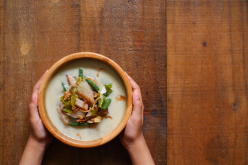 hand holding a bowl of sayur nangka muda against wooden background 